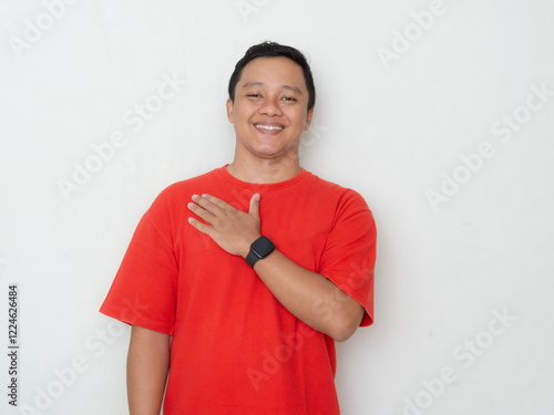 Quadro su tela Smiling young Asian man in red shirt with hand over heart, expressing gratitude or sincerity