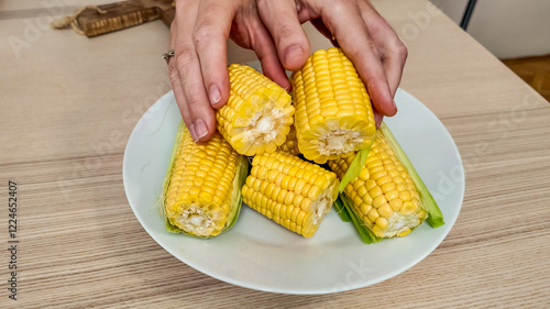 A pair of hands prepares fresh corn on the cob on a white plate, evoking summer harvest and healthy eating