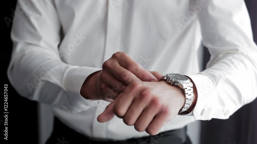 Man Adjusting Watch and Getting Dressed Elegantly, A man in a white dress shirt fastens his wristwatch while preparing for a formal event
