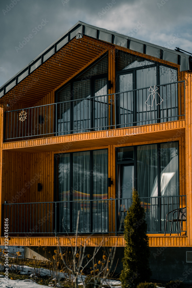 Modern wooden cabin with large windows in snowy landscape during winter afternoon Modern wooden cabin with large windows in snowy landscape during winter afternoon