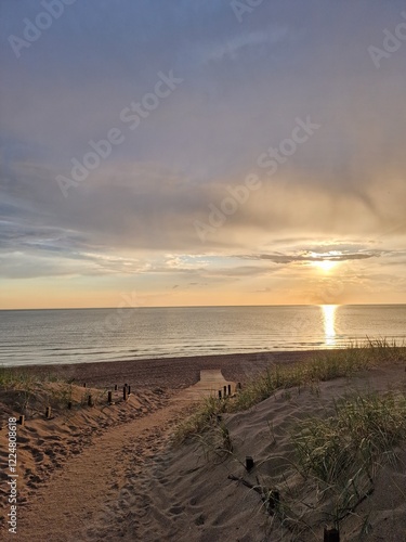 A wooden pathway on a sandy shore to the beach, with the tranquil ocean under a soft golden light, sunset at the beach, minfulness, tranquil ambiance photo