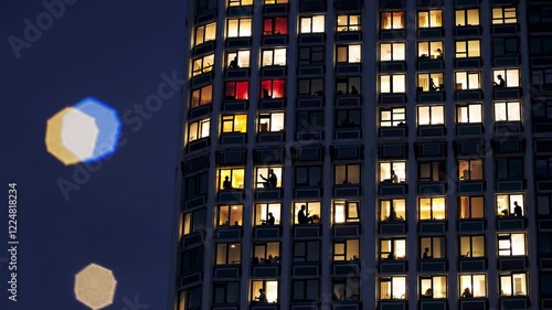 Nighttime urban panorama revealing illuminated skyscraper windows, showcasing silhouetted residents within high rise apartment spaces, capturing metropolitan living dynamics
