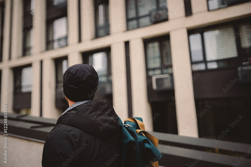 A man walks against the backdrop of modern urban architecture. He is dressed for autumn and has a backpack. A man walks against the backdrop of modern urban architecture. He is dressed for autumn and has a backpack.