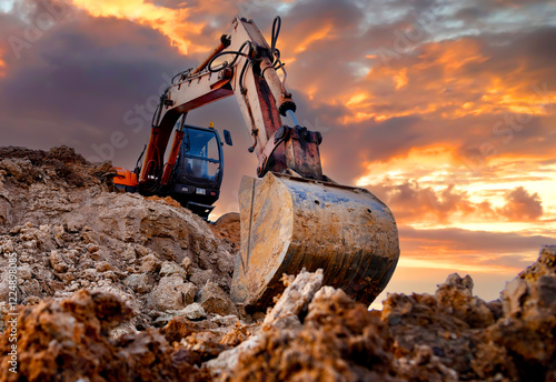 Excavator during earthmoving work at open-pit mining on sunset background. Loader machine with bucket in sand quarry. Backhoe digging th ground for the foundation and for laying sewer pipes