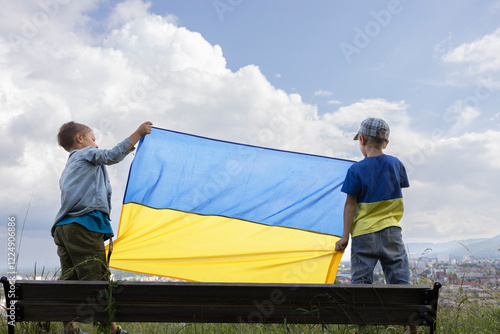 large Ukrainian flag in the hands of two boys against the sky. National symbol of independence. Peace for Ukraine. Children are against war. Pride, patriotic education. photo