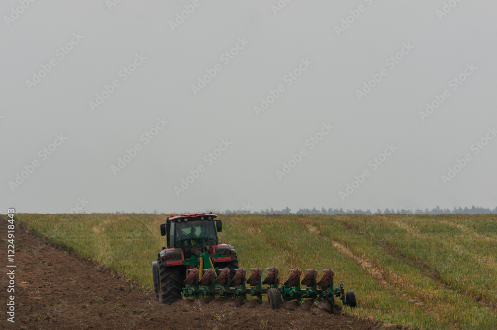 A red tractor is plowing a field, creating a clear division between the tilled soil on the left and the unplowed grass on the right. A red tractor is plowing a field, creating a clear division between the tilled soil on the left and the unplowed grass on the right.