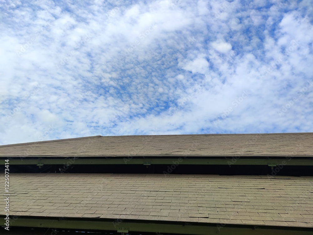 View of a worn asphalt shingle roof under a bright blue sky, showing visible damage and signs of aging on the roofing structure View of a worn asphalt shingle roof under a bright blue sky, showing visible damage and signs of aging on the roofing structure