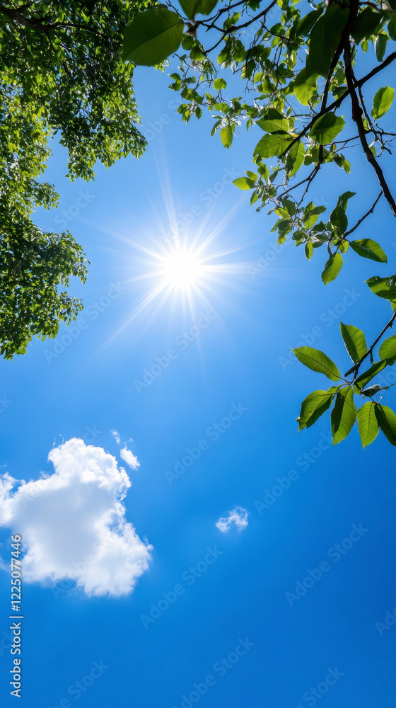 Fototapeta premium An endless azure sky with a radiant sun, viewed from below through lush green tree branches.