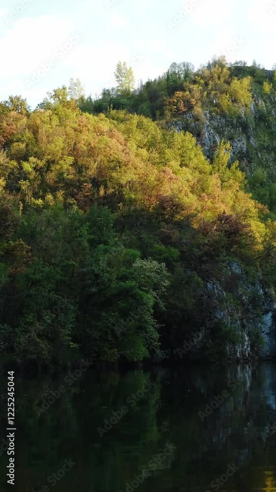 Rocky steep mountains with an autumn forest are reflected in the water on a warm sunny evening. A small mountain lake in a gorge near the town of Uzice in Serbia. 4k vertical footage. Rocky steep mountains with an autumn forest are reflected in the water on a warm sunny evening. A small mountain lake in a gorge near the town of Uzice in Serbia. 4k vertical footage.