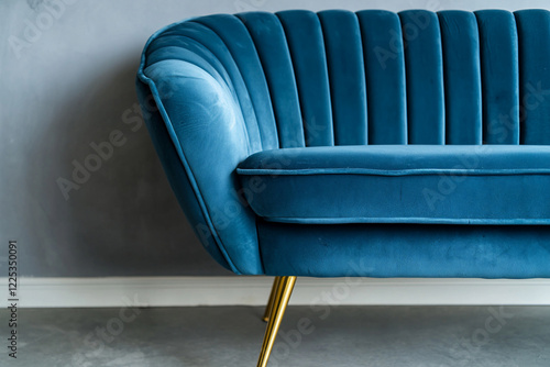 Stylish blue velvet sofa with gold legs against a minimalist gray wall, enhancing modern interior decor photo