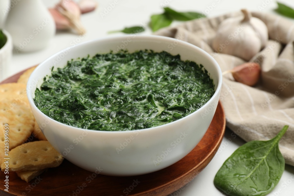 Delicious spinach sauce in bowl, crackers and garlic on white table, closeup Delicious spinach sauce in bowl, crackers and garlic on white table, closeup