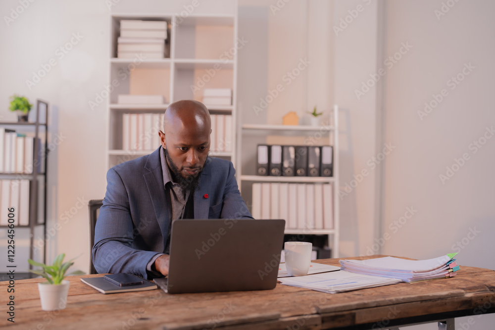 Focused businessman working diligently on a laptop in a modern office, surrounded by stacks of paperwork and office supplies, maintaining concentration on important tasks Focused businessman working diligently on a laptop in a modern office, surrounded by stacks of paperwork and office supplies, maintaining concentration on important tasks