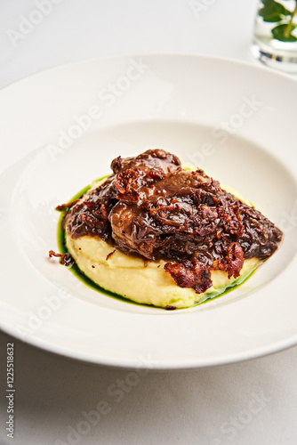 A beautifully presented dish showcases succulent meat resting on smooth, creamy puree, adorned with a rich sauce. The setting is refined, perfect for a gourmet dining experience photo