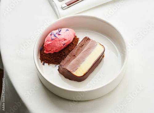 A delicate dessert is presented on a white plate, featuring a layered chocolate cake beside a scoop of pink sorbet, garnished with lavender. Enjoying a refined dining experience photo