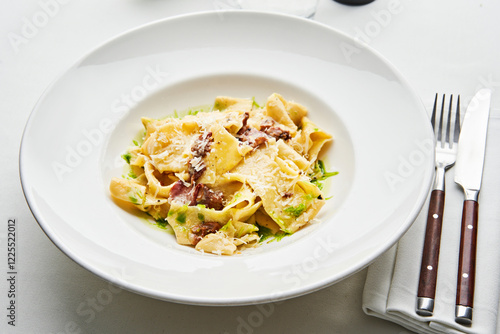 A plate of freshly made pasta with bacon is presented beautifully, topped with savory sauce and sprinkled with cheese. Greens add color to the dish, making it appealing photo