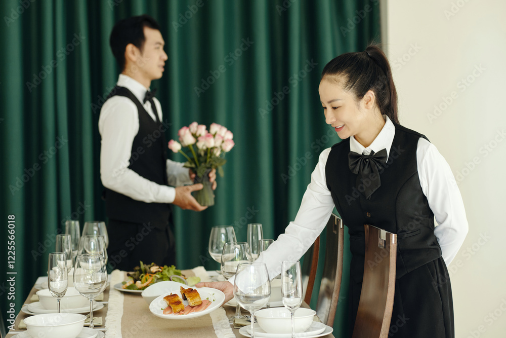 Professional waiters in uniform setting the dining table with flowers and dishes during catering service Professional waiters in uniform setting the dining table with flowers and dishes during catering service