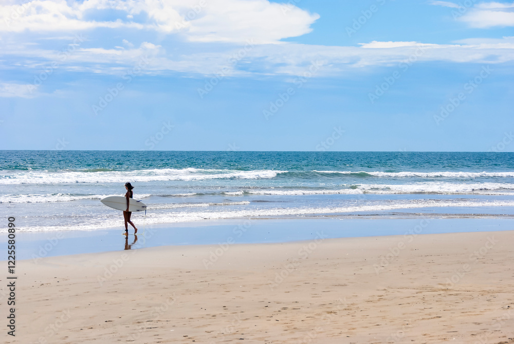 Young woman surfer walking along the beach with a surfboard on a sunny day Young woman surfer walking along the beach with a surfboard on a sunny day