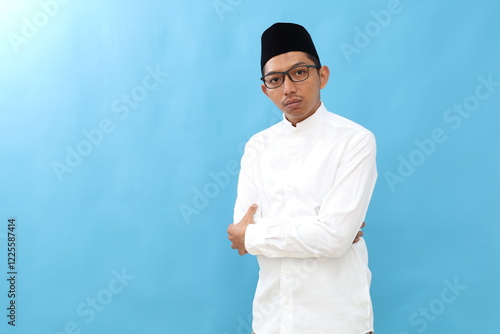 Asian man wearing typical arab clothes isolated on blue background who feels confident, crossing arms with determination. photo