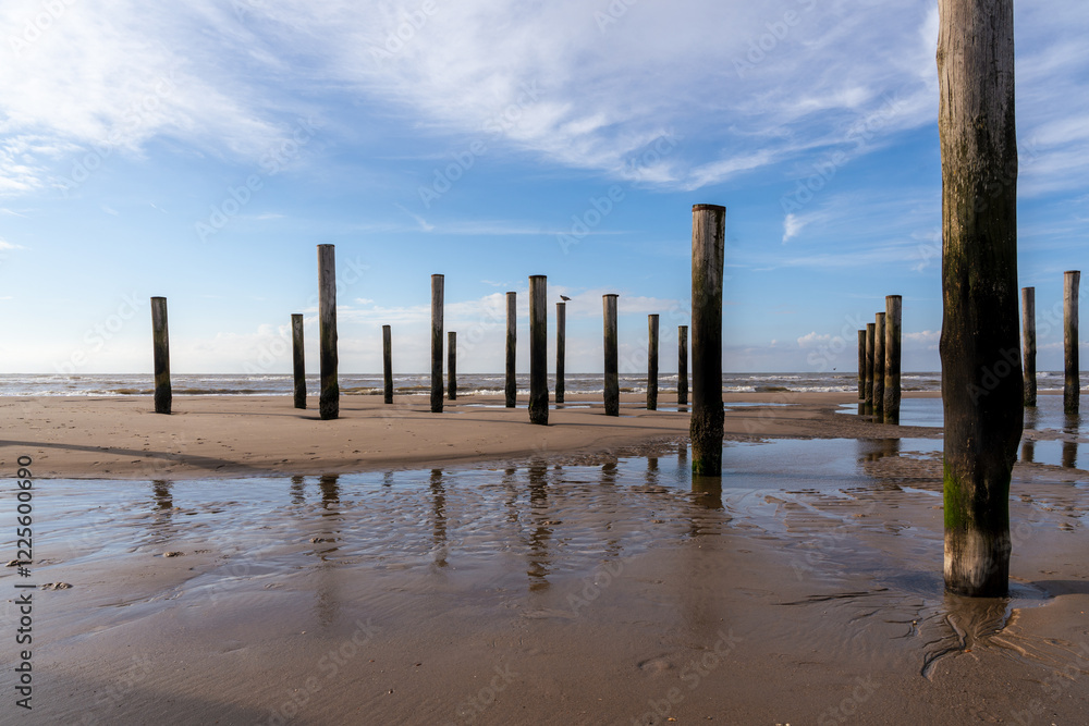 Holzpfähle am Sandstrand der Nordsee vor blauen Himmel mit Wolken und Wellen Holzpfähle am Sandstrand der Nordsee vor blauen Himmel mit Wolken und Wellen