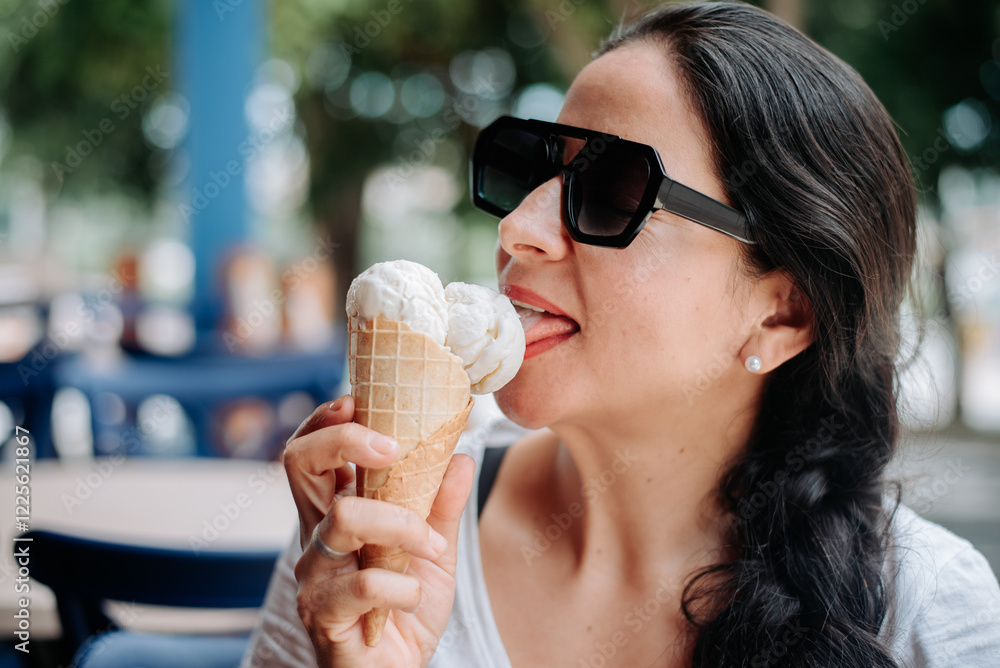 A happy woman eating ice cream while wearing sunglasses. A happy woman eating ice cream while wearing sunglasses.