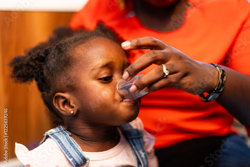 Canvas Print Loving African mother giving her child syrup medicine at home.