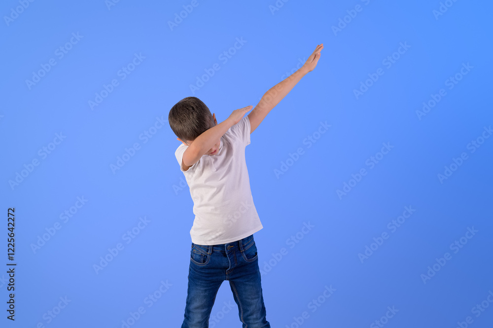 Portrait of elementary boy with arms raised dabbing while dancing against isolated blue background Portrait of elementary boy with arms raised dabbing while dancing against isolated blue background