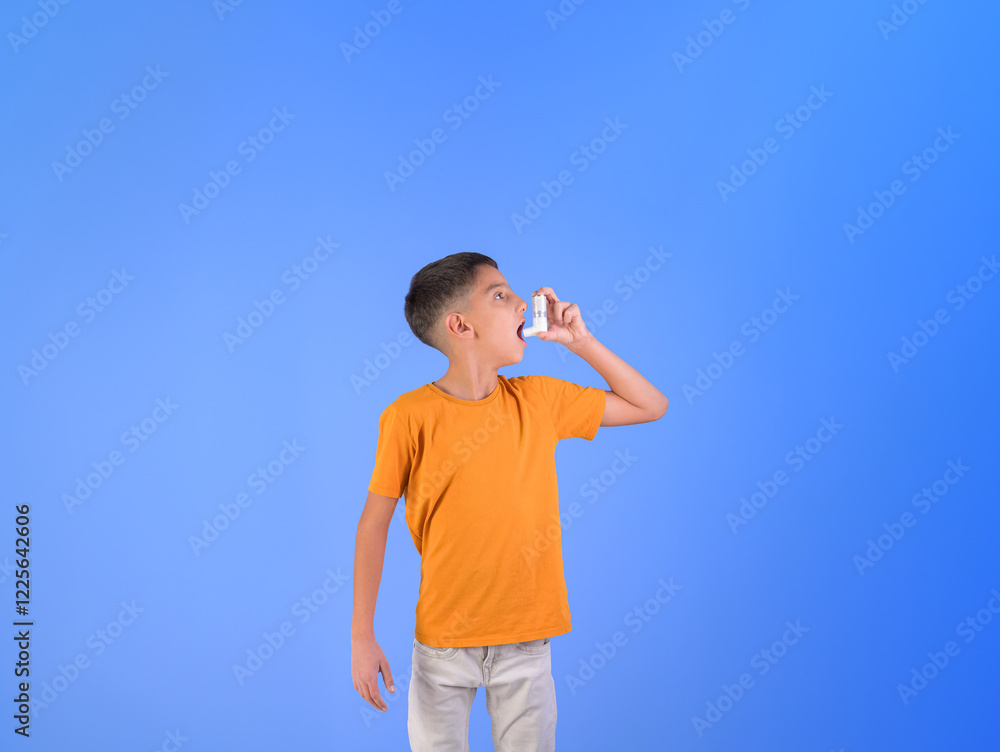 Portrait of asthmatic boy inhaling through asthma pump while standing against isolated blue background Portrait of asthmatic boy inhaling through asthma pump while standing against isolated blue background