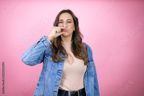 Tableau sur toile Young beautiful woman wearing denim jacket over isolated pink background mouth and lips shut as zip with fingers