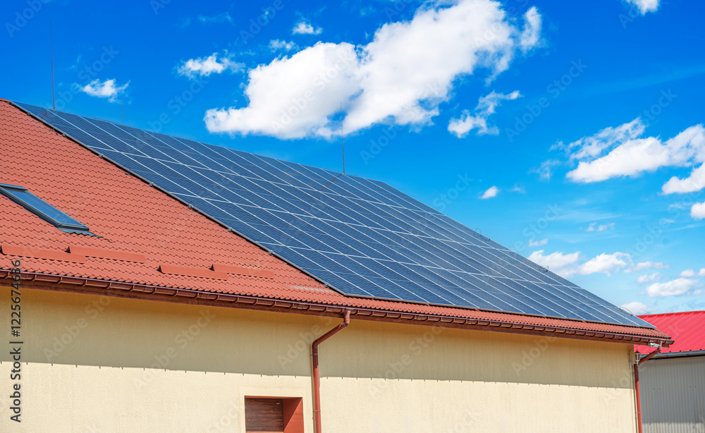 A set of solar panels is installed on the roof of a building with red tiles under a clear blue sky.