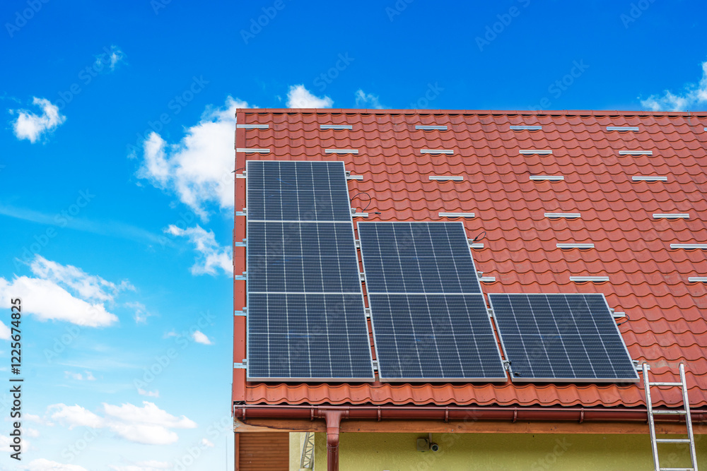 A set of solar panels is installed on the roof of a building with red tiles under a clear blue sky.