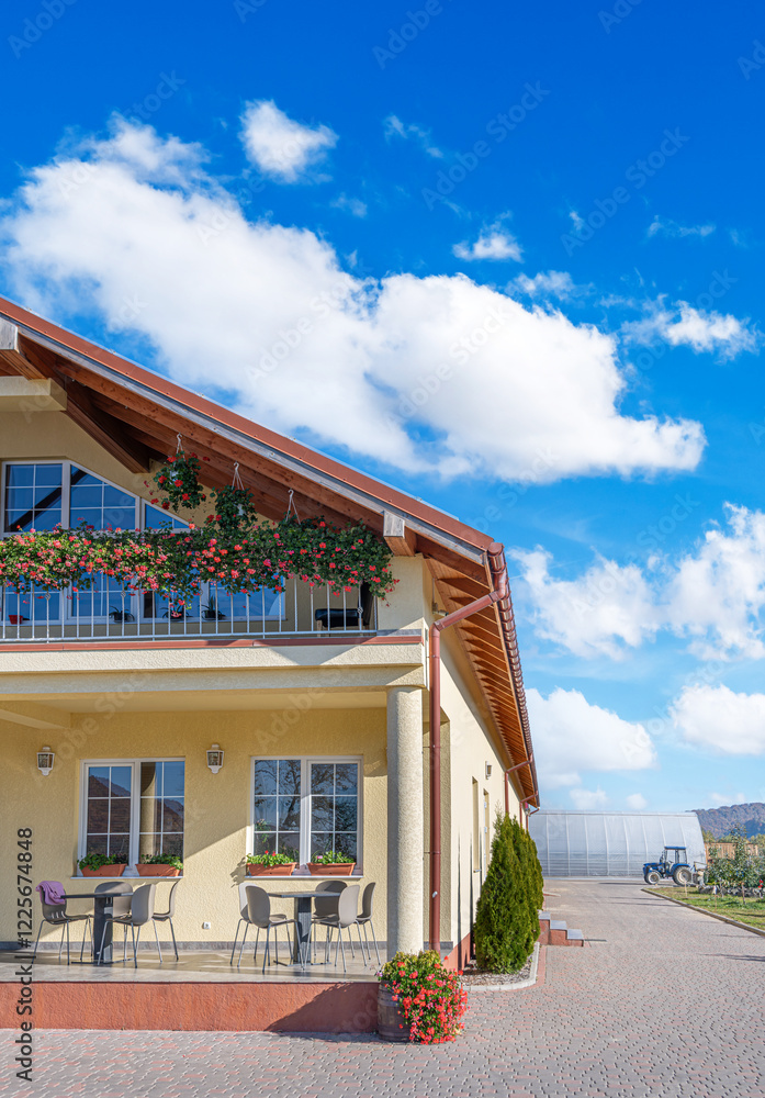 A charming countryside house with a cozy outdoor terrace and a balcony decorated with vibrant red geraniums.