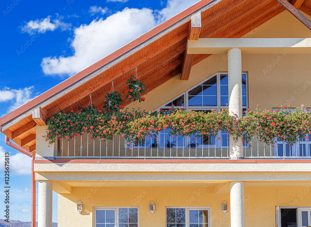A charming countryside house with a cozy outdoor terrace and a balcony decorated with vibrant red geraniums.