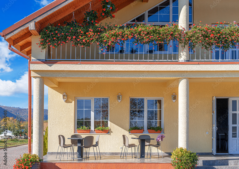 A charming countryside house with a cozy outdoor terrace and a balcony decorated with vibrant red geraniums.