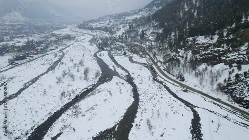 Wide angle aerial drone shot flying over the frozen Lidder river with the snow covered himalaya mountains on the side with road at the base and small villages in gulmarg kashmir photo