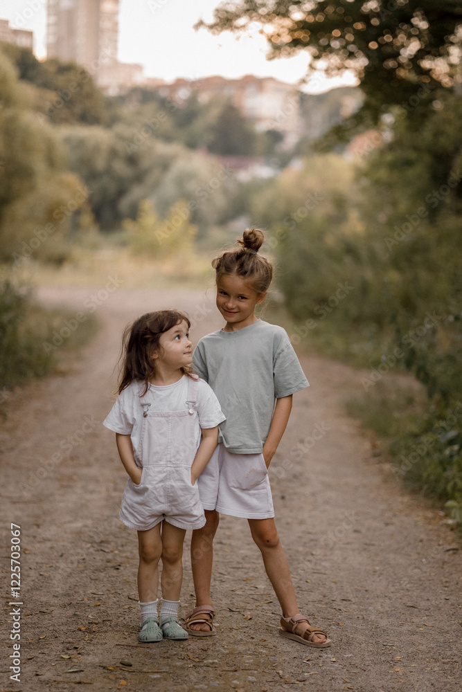 Two sisters aged 5 and 3 play in a park against the backdrop of the city, running races and playing catch-up Two sisters aged 5 and 3 play in a park against the backdrop of the city, running races and playing catch-up