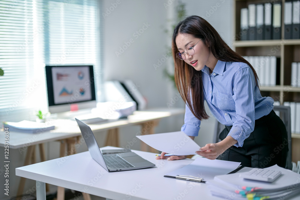 A woman is sitting at a desk with a laptop and papers in front of her A woman is sitting at a desk with a laptop and papers in front of her