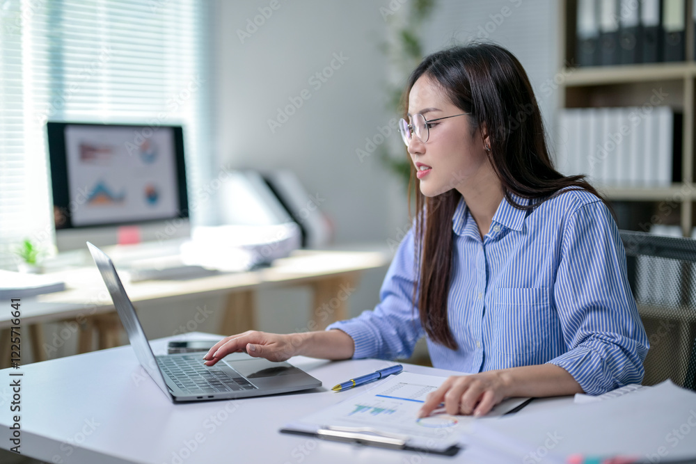 A woman is sitting at a desk with a laptop and a stack of papers A woman is sitting at a desk with a laptop and a stack of papers