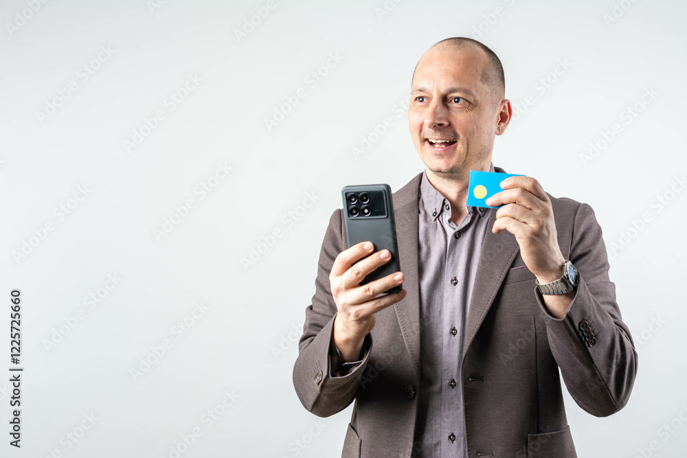 Shot of cheerful businessman holding mobile and credit card, while standing isolated. Shot of cheerful businessman holding mobile and credit card, while standing isolated.