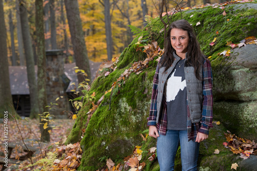 Cute young brunette woman poses for photo in forest on top of boulder - autumn photo