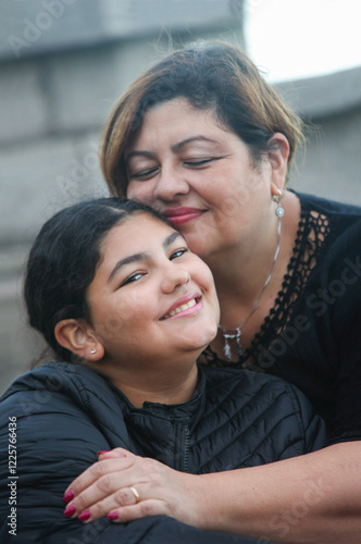 portrait of happy hispanic mother embracing  her teenage daughter. outdoors on cloudy autumn day 