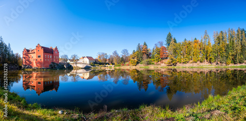 Obraz na płótnie Panoramic view of Cervena Lhota Castle in the Czech Republic, surrounded by a lake reflecting its image. Autumn trees in vibrant colors and sunny weather create a picturesque, serene scene. w salonie