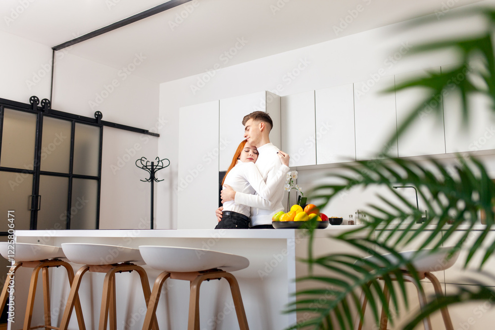 young couple in love stands in white modern new kitchen at home and hugging, girl and guy rejoice together and advertise furniture in the kitchen young couple in love stands in white modern new kitchen at home and hugging, girl and guy rejoice together and advertise furniture in the kitchen