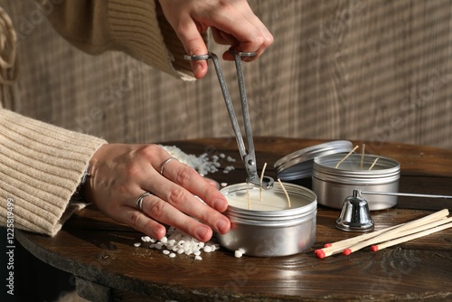 Woman cutting soy candle wick with trimmer at wooden table, closeup photo