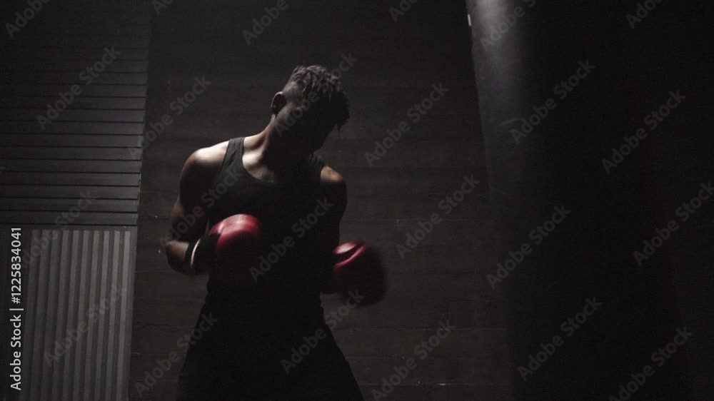 african american young boxer training in dark gym and hitting punching bag with gloves, strong man doing sports and training endurance african american young boxer training in dark gym and hitting punching bag with gloves, strong man doing sports and training endurance