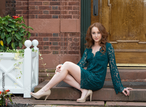 Stunning young woman with red hair poses in green lace trimmed dress in front of wooden entry door - sitting on front stoop photo