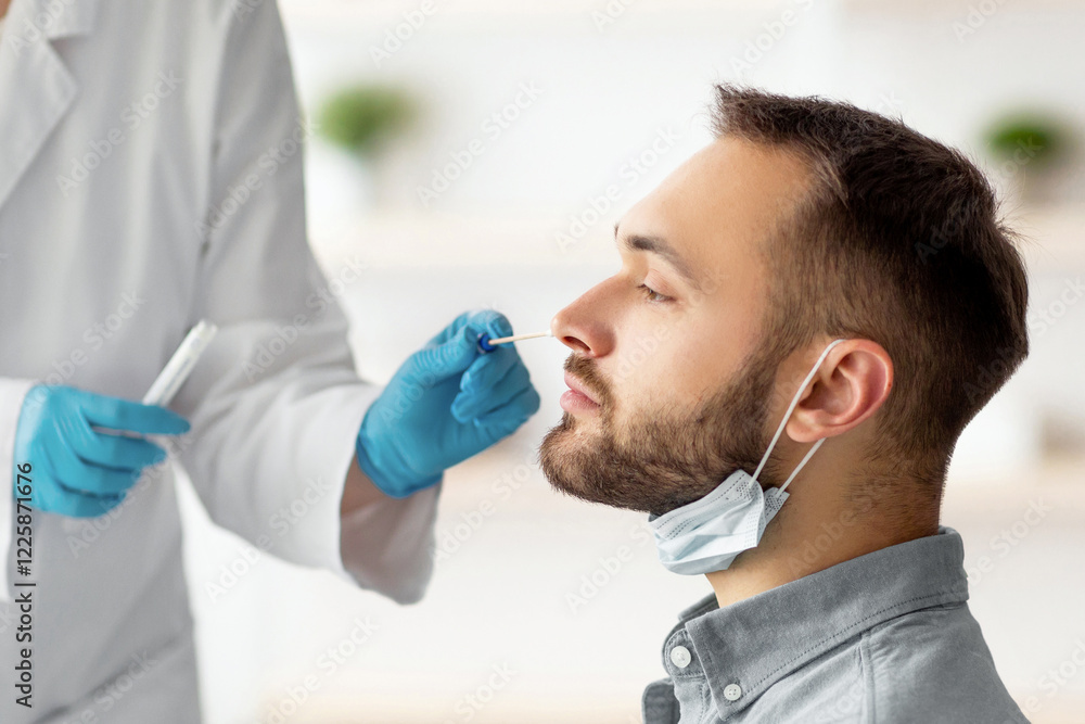Naklejka premium Covid diagnostic procedure. Doctor making nasal PCR test for young Caucasian man, using sterile swab stick at home. Millennial guy undergoing coronavirus analysis, checking health