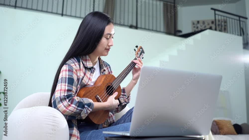 young asian woman learning to play the ukulele online on laptop, korean girl learning to play musical instrument from video lesson young asian woman learning to play the ukulele online on laptop, korean girl learning to play musical instrument from video lesson