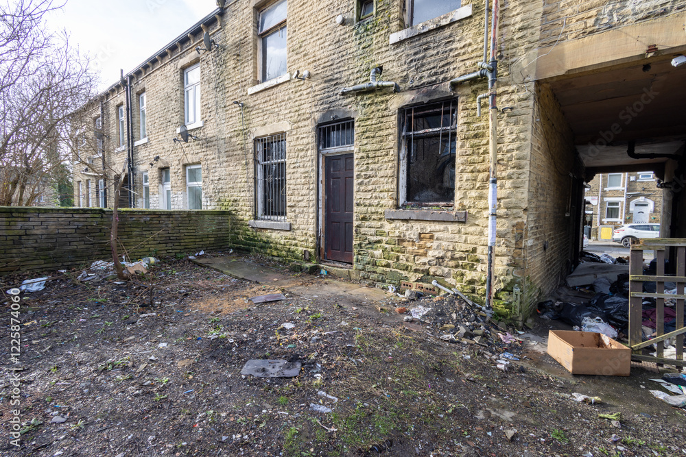 Photo taken of an extremely run down property that has had a massive fire showing the outside of the property that is in need of repair and the neglected front garden of the house