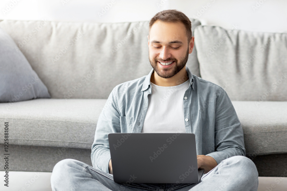 Full length of happy Caucasian man sitting cross legged on floor, using laptop pc, working online from home office. Cheerful millennial freelancer making remote business project indoors Full length of happy Caucasian man sitting cross legged on floor, using laptop pc, working online from home office. Cheerful millennial freelancer making remote business project indoors
