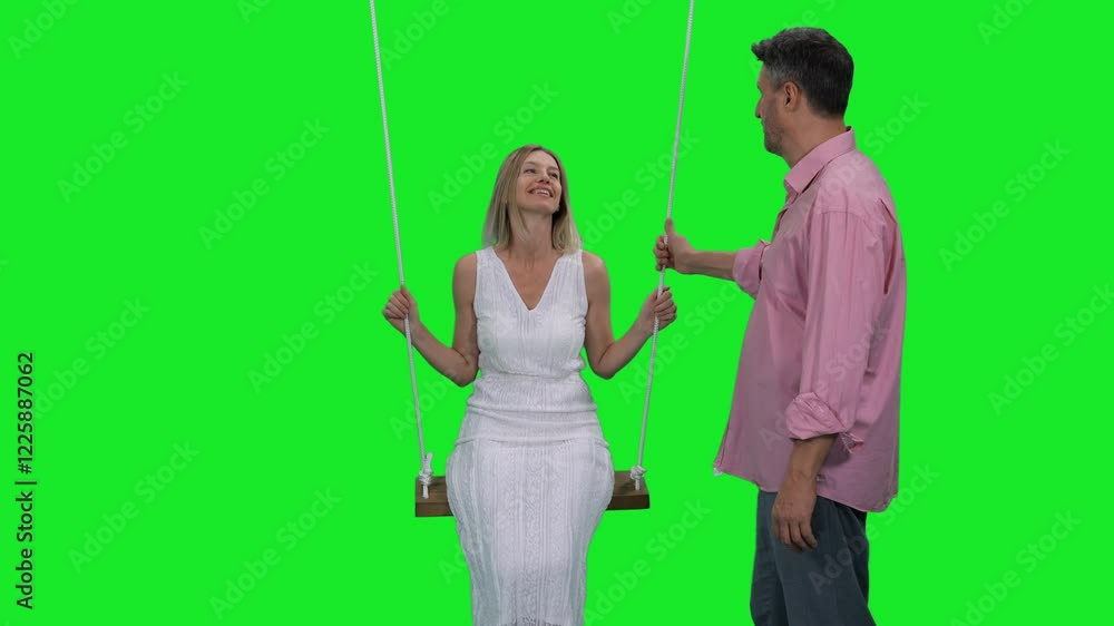 Slow motion of laughing woman in white dress on hanging swing her husband standing nearby on green chroma key background, 4k pre-keyed footage Slow motion of laughing woman in white dress on hanging swing her husband standing nearby on green chroma key background, 4k pre-keyed footage
